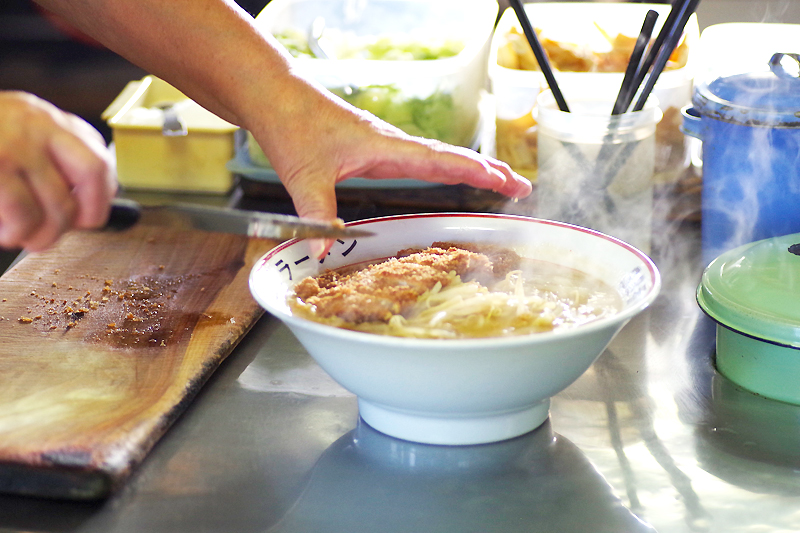 ラーメンにカツをのせている様子の写真